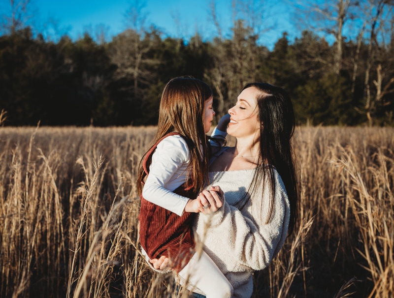 Family photography, a woman holds her young daughter and they draw face to face joyfully
